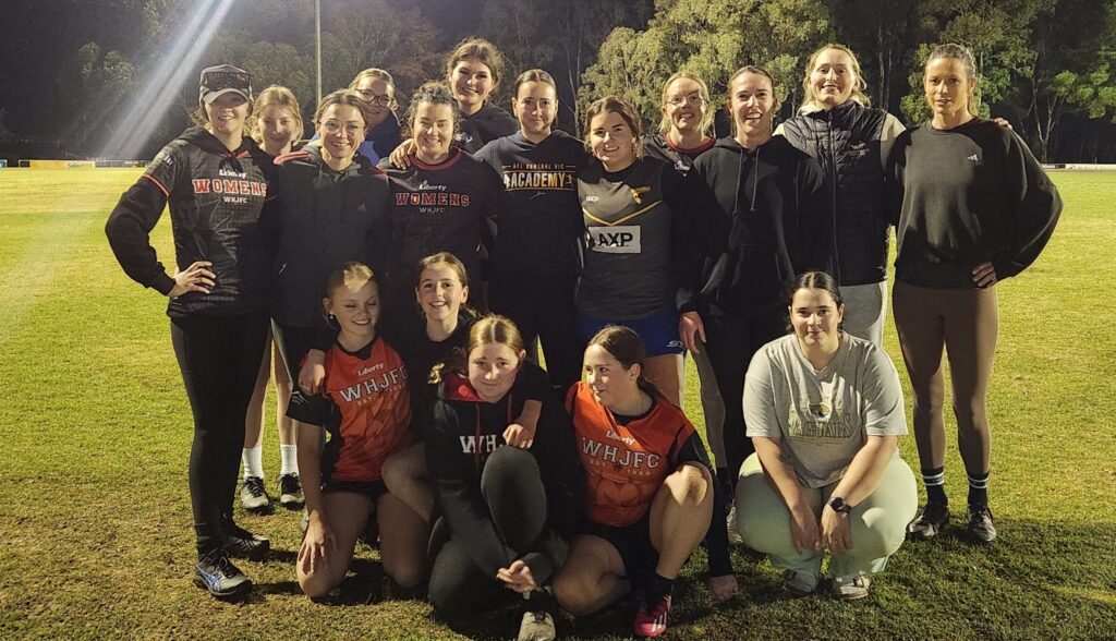 White Hills Senior Womens team with Under 12 Girls team huddled together on a footy oval
